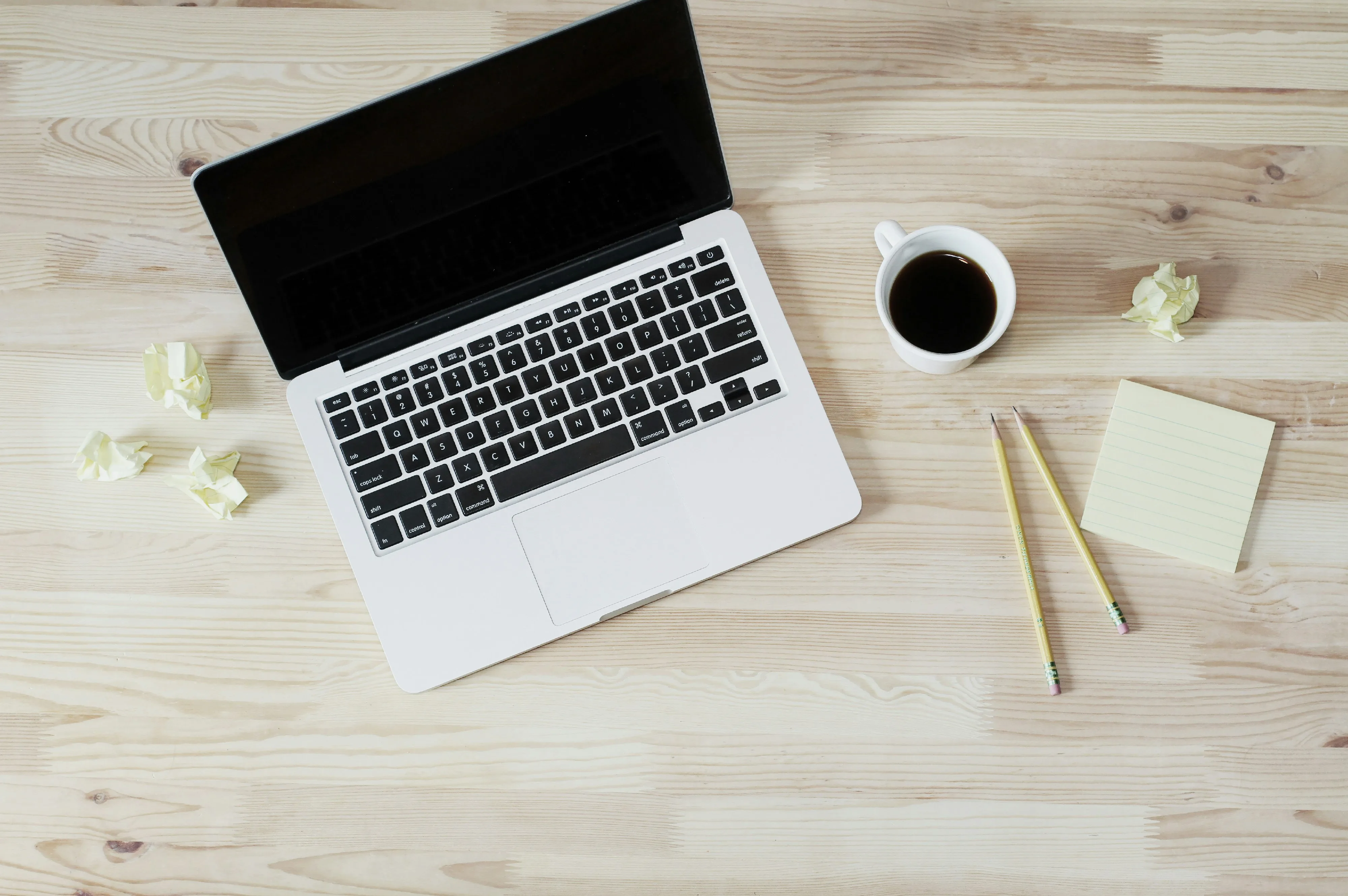 Ordinateur portable vu de haut sur un bureau en bois avec café et bloc-notes